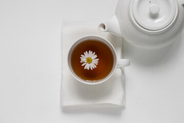 White cup with tea from chamomile useful natural on a white background near a white teapot
