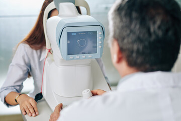 Ophthalmologist using modern equipment when checking eyesight of young female specialist