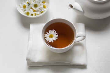 Obraz na płótnie Canvas White cup with healthy natural chamomile tea on a white background near a white teapot and chamomile