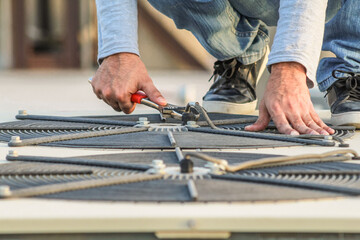a professional electrician man is fixing the heavy air conditioner by his tools on the roof top and wearing blue color of uniform and head cap