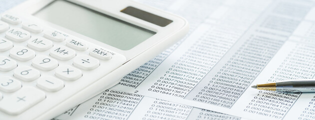 Naklejka na ściany i meble Finance and business concept. White calculator on financial graphs on office desk, paperwork binder, glasses. Accounting budgeting or market analysis. Web banner with copy space. Minimal monochrome