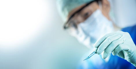 close up of the surgeon's hand holding a scalpel and blurred female doctor's face in the background with copy space, concept of surgical operations, hospitals and clinics staff - obrazy, fototapety, plakaty