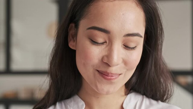 Close up view of Smiling elegant pretty asian woman becoming shy and looking at the camera at home