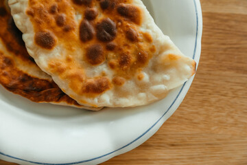 Homemade gold cheburek with meat on a white plate on wooden table