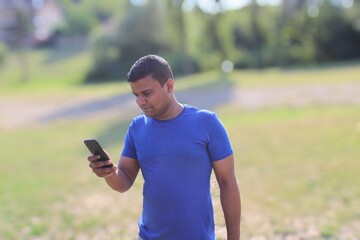 Fototapeta premium young smiling man looking at his mobile in happy mood outdoor in park
