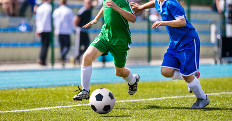 Obraz premium Football Players in Running Duel. Forward and Defense Player Compete for the Ball. Sports Stadium in the Background