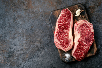 Two raw new York steaks on a chopping Board with seasonings and garlic. Wagyu meat for grilling, top view and copy space