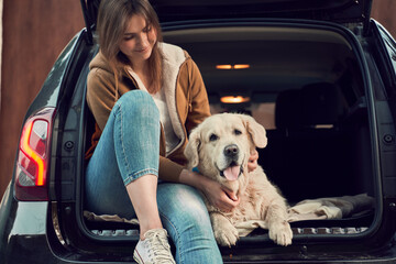 Smiling woman with golden retriever sit in open trunk of black car