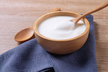 Yogurt in wooden bowl with spoon and blue cotton on table background .