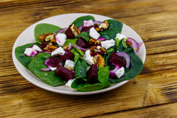 Tasty spinach salad with boiled beetroot, feta cheese, walnut and red onion on wooden table. Healthy vegetarian food