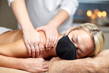 Obraz na płótnie Canvas beauty and health safety concept - woman wearing face medical mask for protection from virus lying with closed eyes and having hand massage in spa