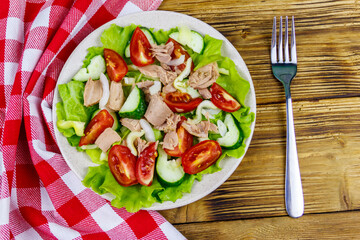 Tasty tuna salad with lettuce and fresh vegetables on wooden table. Top view