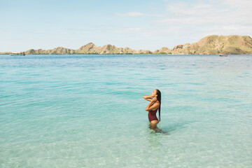 Woman in red swimsuit enjoying in transparent turquoise ocean water with mountain view. Travel and vacations concept. Beauty and wellness. Tropical background with empty space.