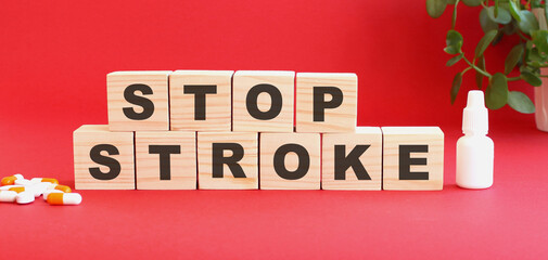 Fototapeta premium The words STOP STROKE is made of wooden cubes on a red background with medical drugs. Medical concept.