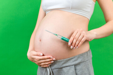 Close up of pregnant woman holding a syringe against her belly at colorful background with copy space. Injection during pregnancy concept
