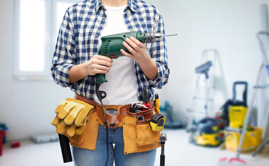 Fototapeta na wymiar repair, construction and building concept - close up of woman or builder with working tools on belt with electric drill or perforator over utility room background
