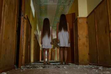 two girls in white dresses with long hair hold a Teddy bear together in the middle of a creepy...