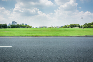 Empty asphalt road and green lawn under blue sky