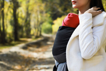 Beautiful young mother with her infant baby in sling outdoor. Babywearing concept