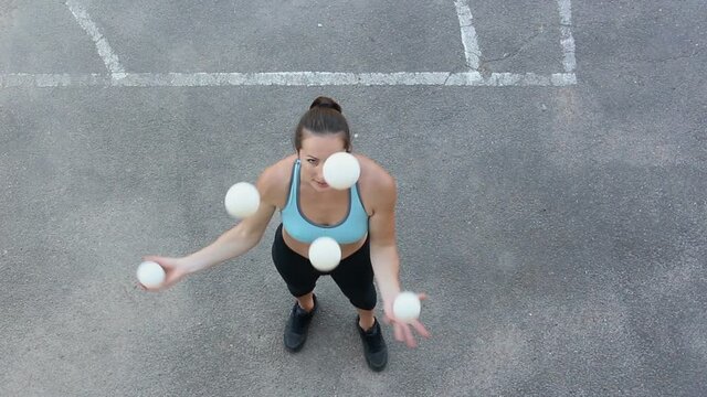 A professional juggler juggles with white balls. An attractive girl juggler trains her juggling skills. A professional circus actress juggles with white balls on the street.