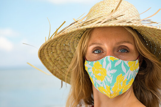 Funny portrait of young woman in straw hat on tropical sea beach. New rules to wear cloth face covering mask at public places due coronavirus COVID 19. Family holiday with kids, travel at summer 2020.