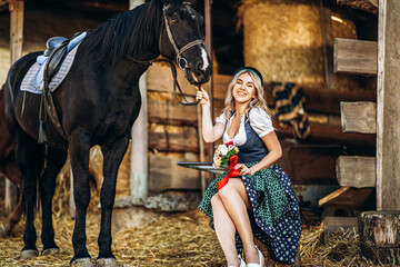 Fototapeta na wymiar Pretty blonde in traditional dress take care of big black horse at the farm