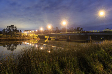 Obraz premium A road bridge crossing a river in the countryside. Photographed at night while brightly lit up with streetlights