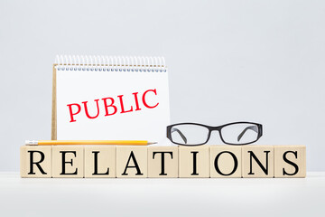 Public relations text concept. Building blocks with notepad, pencil and eyeglasses. Business or...