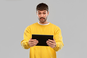 technology and people concept - surprised young man in yellow sweatshirt with tablet pc computer over grey background