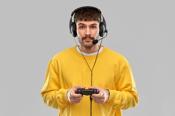 technology, gaming and people concept - young man or gamer in headphones with gamepad playing and streaming video game over grey background © Syda Productions