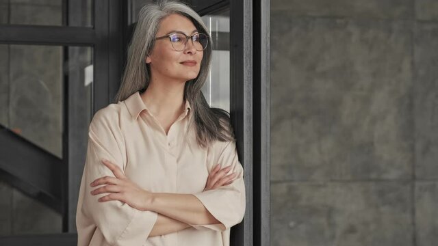 An attractive mature woman wearing glasses is standing in the living and looking to the side room at home