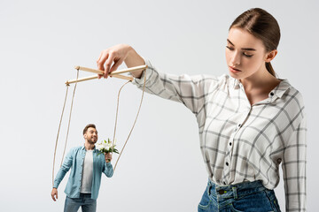 female puppeteer holding male marionette with flowers isolated on grey