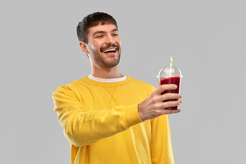 drinks and people concept - happy smiling young man holding tomato juice in takeaway plastic cup with paper straw over grey background