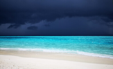 Tropical Maldives beach with turquoise blue water and rain sky.
