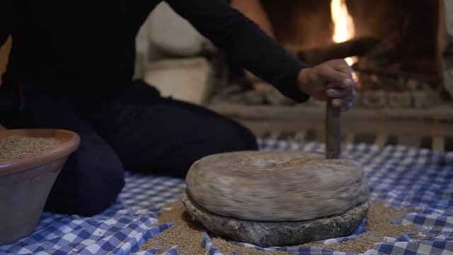 The ancient quern stone hand mill with grain. The woman grinds the grain into flour with the help of a millstone. Men's hands rotates a millstone. Old grinding stones turned by human hands