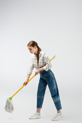 attractive girl posing like puppet with mop and frying pan isolated on grey