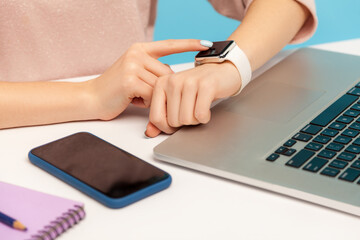 Fototapeta premium Closeup of woman employee looking at smart watch on her hand while working on laptop in office, checking hour to take break, touching screen to turn off alarm clock. indoor studio shot, isolated