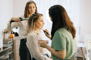 Wedding makeup artist making fashion make-up for beautiful bride in lighting dressing room. Concept of backstage work.