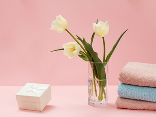 Bouquet of yellow tulips in vase with towels on a pink background.