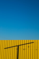 background image clear blue sky yellow fence where the shadow of the post is a play of light and shadows in the summer in Sunny weather outdoors