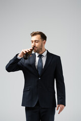 handsome businessman in suit drinking beer isolated on grey