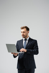 handsome businessman in suit using laptop isolated on grey