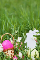Colorful easter eggs, wooden rabbit and flowers on fresh spring grass in the garden. Close up of easter egg in a basket.