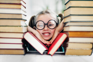 Preschool age girl with dimples in big funny glasses among a pile of books