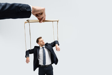 cropped view of puppeteer holding businessman marionette on strings isolated on grey