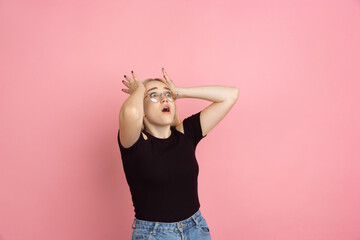 Crazy shocked, wondered. Portrait of young woman with bright emotions on coral pink studio background. Blonde female model. Concept of human emotions, facial expression, sales, advertising, youth.