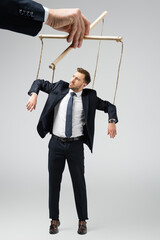 cropped view of puppeteer holding businessman marionette on strings isolated on grey