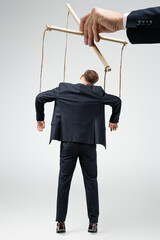 cropped view of puppeteer holding businessman marionette on strings isolated on grey