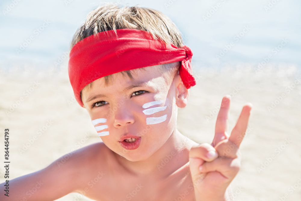 Wall mural Sunscreen (suntan lotion) is on hipster boy face before tanning during summer holiday on beach. Child (kid) is holding container of sunscreen (not far from Trieste, Italy).