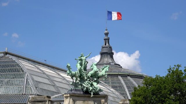 French flag waving on top of Grand Palais with bronze quadriga statue "Harmony Triumphing over Discord" in the foreground (by Georges Recipon (1860 - 1920) - Paris, France